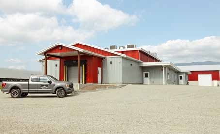 A red and grey abattoir building by a large gravel parking lot. A grey king cab truck is parked in front of the building.