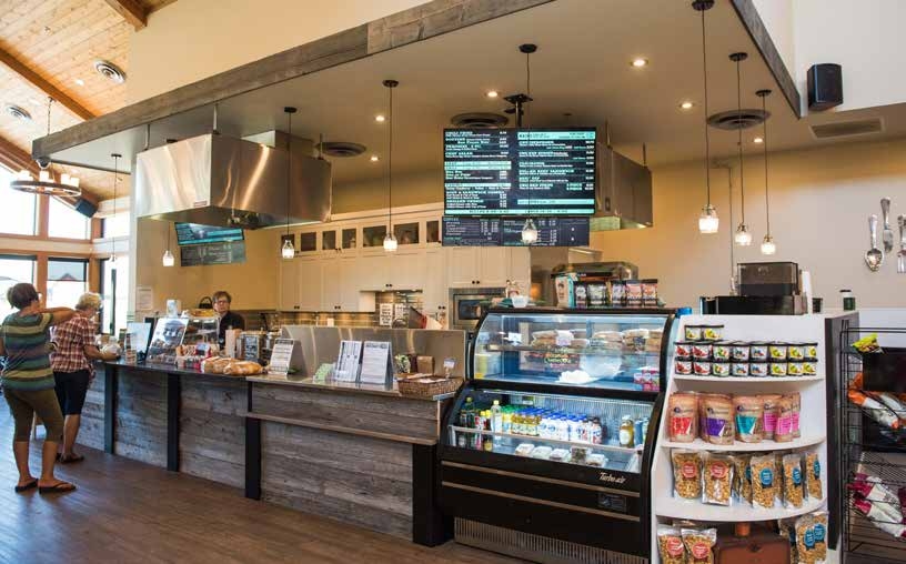 A café counter with people waiting in a queue to order. The café is bright and has displays of products and large menus behind the counter. 