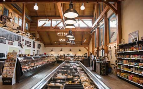 The inside of a boutique shop with vaulted wooden ceilings. Rows of product shelves are along the walls along with a butcher’s counter display. 