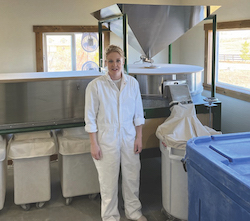 Woman in white coveralls standing in front of a stone flour mill