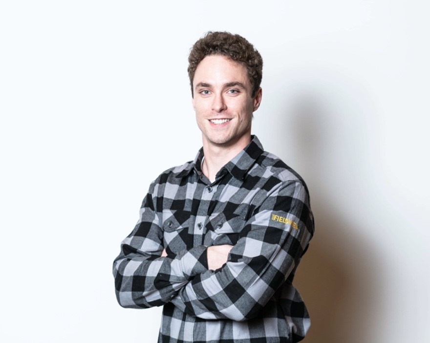 A professional portrait of a man smiling with his arms crossed. He is wearing a black and grey checkered button up shirt. 