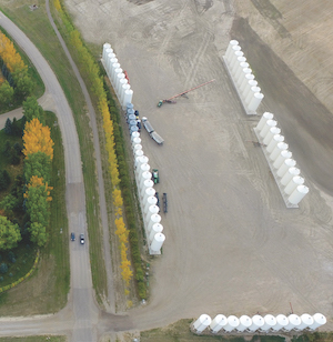 An aerial view of Stamp’s Seed operation, with many white silos lined up. Trucks and trailers are near the silos off a rural road.