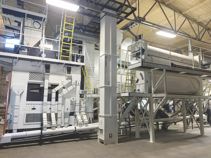 Inside Stamp Seeds seed cleaning plant, an industrial warehouse with many large pieces of machinery that are grey and white.